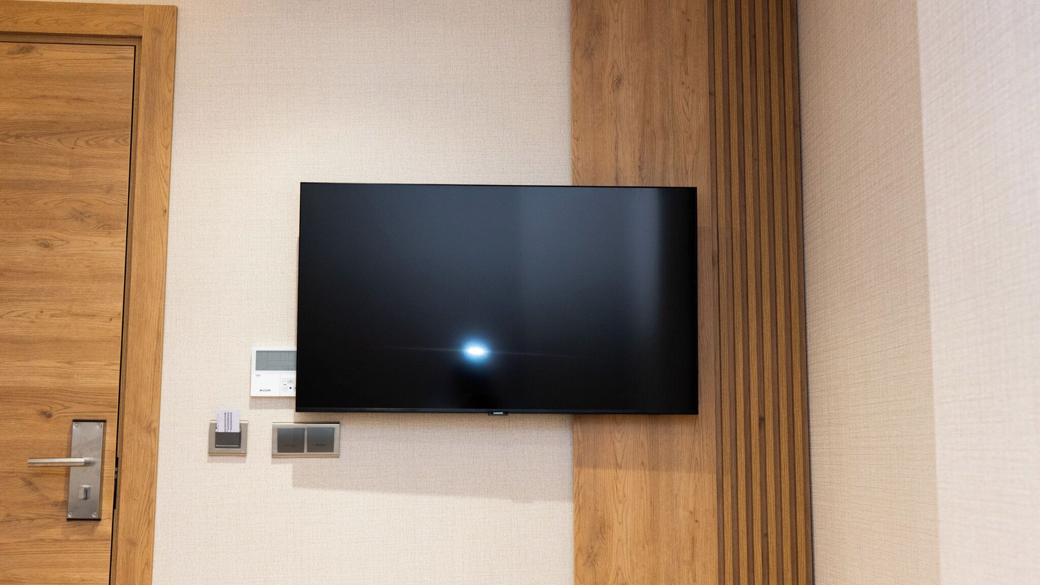 A flat-screen TV mounted on a wall with a wooden door to the left and a textured wall to the right.