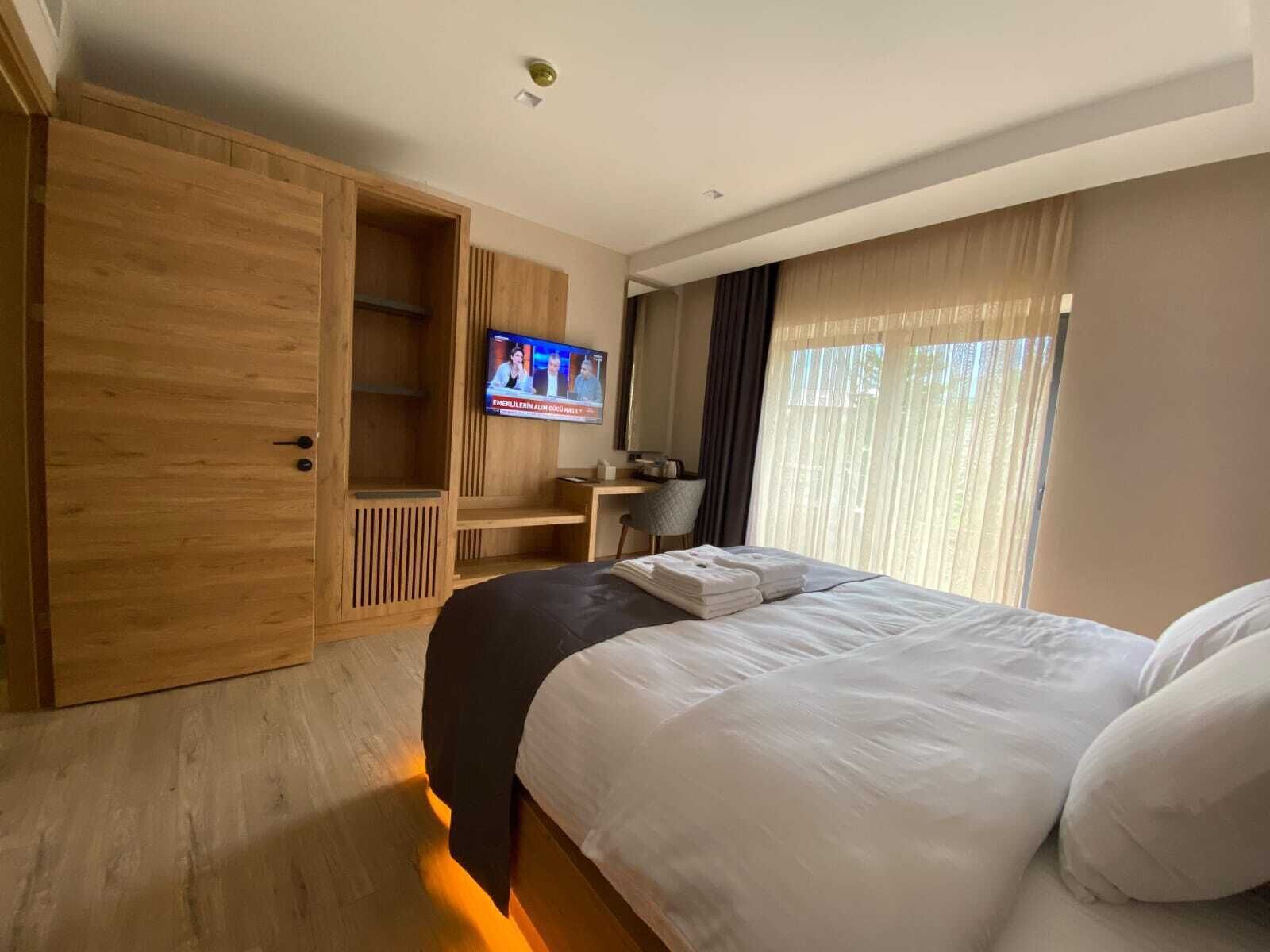 A hotel room with a large bed, a wooden wardrobe, a TV, a desk, and a window with curtains.