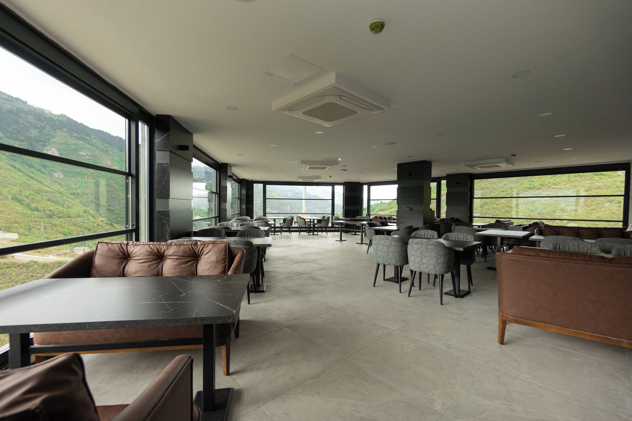 Un espacio interior amplio con diversas opciones de asientos, ventanas grandes que ofrecen vistas a colinas verdes y un diseño de techo moderno.