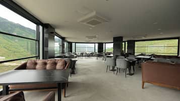 Un espacio interior amplio con diversas opciones de asientos, ventanas grandes que ofrecen vistas a colinas verdes y un diseño de techo moderno.