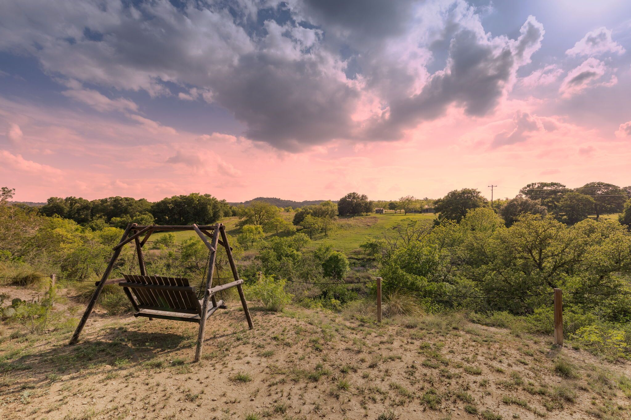 A swing set in a natural landscape with trees and a cloudy sky.
