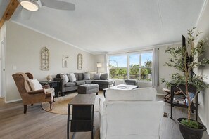 A spacious living room with a sectional sofa, a coffee table, and a fireplace. There is a large window providing a view of the outdoors.