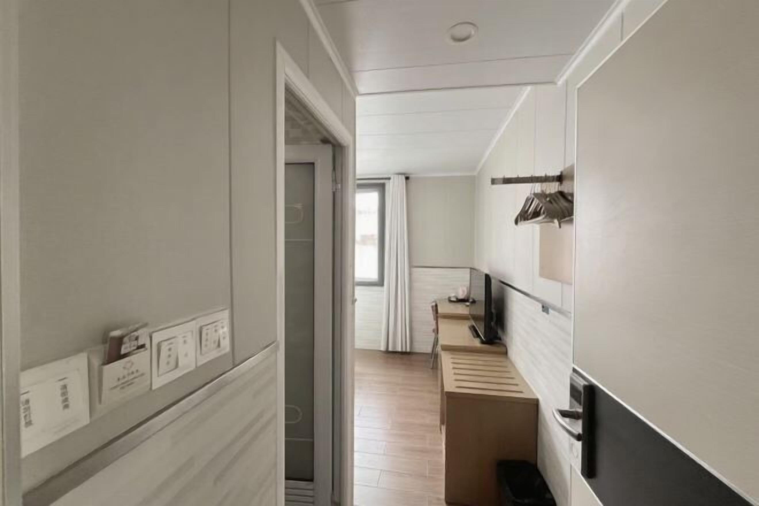 Um corredor com chão de madeira, uma porta que dá para um quarto e uma pequena mesa com uma cadeira.