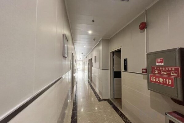A hotel corridor with doors, a fire alarm, and a sign indicating the fire exit. - Yayuan Hostel (Guangzhou)