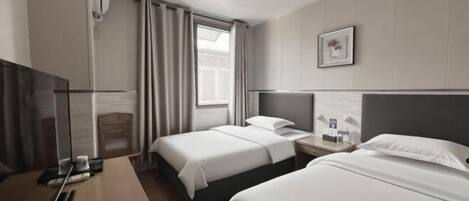 A hotel room with two beds, a TV, a desk, and a window with curtains.