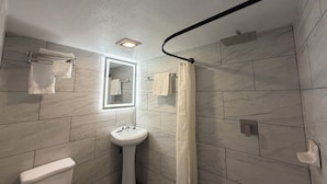 A bathroom with a toilet, sink, mirror, and shower curtain. - Ponca Motel (Abilene)