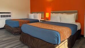 A hotel room with two beds, an air conditioning unit, a nightstand with a lamp, and a wall-mounted light fixture. - Ponca Motel (Abilene)