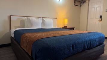 A hotel room with a bed, a nightstand, a lamp, and a door.