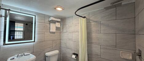 A bathroom with a sink, toilet, shower curtain, and a window with blinds.