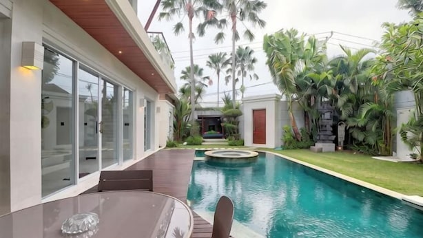 A modern poolside area with a glass table and chairs, surrounded by lush greenery and a clear swimming pool. - Luxury - Villa Ron - Central Seminyak (Bali)
