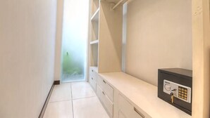 A narrow hallway with a door leading to a bright area, a white tiled floor, and a small safe on a counter. - Luxury - Villa Ron - Central Seminyak (Bali)