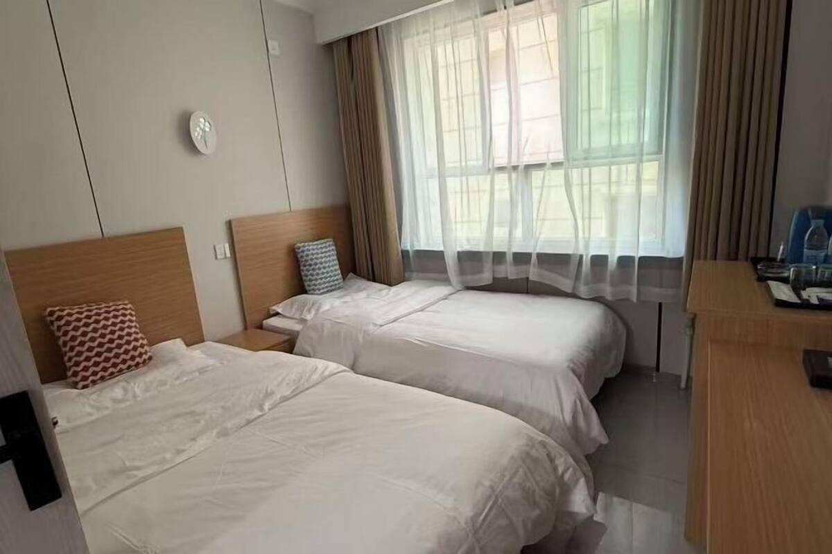 Une chambre d’hôtel avec deux lits, un bureau et une fenêtre avec des rideaux.