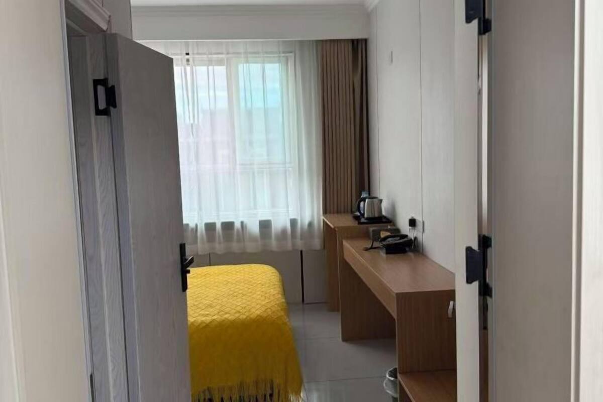 Une chambre d’hôtel avec un lit, un bureau, une chaise, une fenêtre avec des rideaux et une porte.