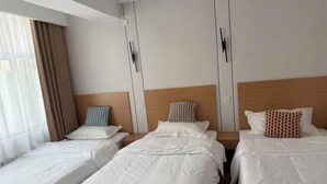 A hotel room with three single beds, a wooden headboard, and a large window with curtains.