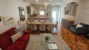 A spacious living area with a red sofa, a glass coffee table, and a dining area with a kitchen in the background.