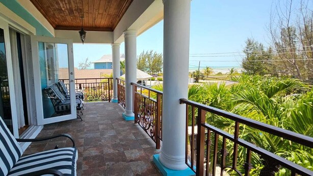 A covered balcony with a striped sofa, a dining table with chairs, and a view of the ocean.