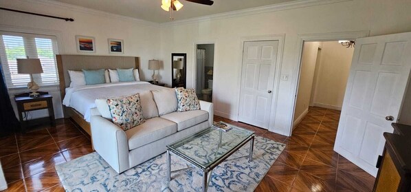 A bedroom with a bed, a sofa, a glass coffee table, and a door.