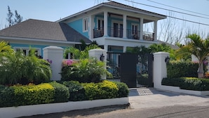 A two-story house with a balcony, surrounded by well-maintained gardens and a gated entrance.