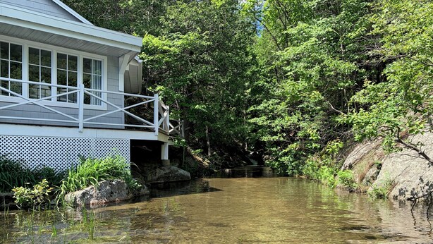 A house with a porch overlooking a clear stream. - Cozy, renovated rustic cottage on the shore of beautiful navigable lake
 (Labelle)