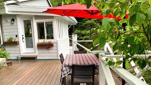 A wooden deck with a table and chairs, a red umbrella, and a white fence. - Cozy, renovated rustic cottage on the shore of beautiful navigable lake
 (Labelle)