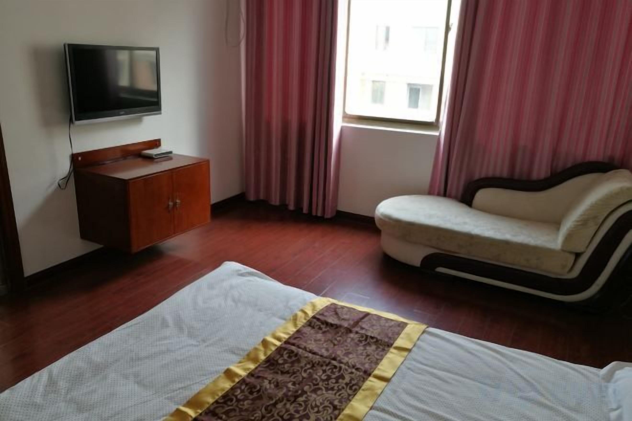 A hotel room with a bed, a sofa, a television on a wooden cabinet, and a window with curtains.