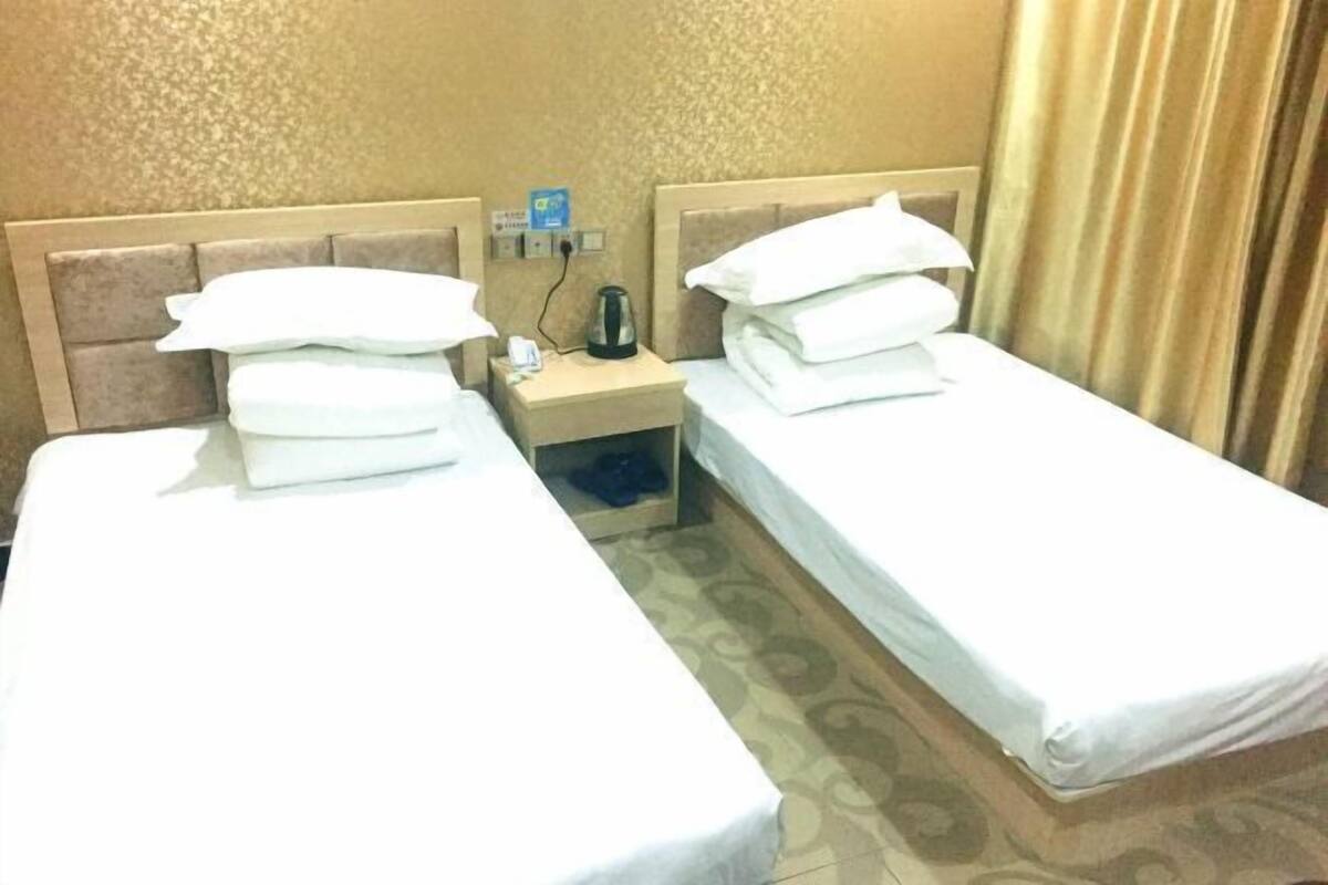 A hotel room with two single beds, a nightstand with a lamp, and a small table with a cup and a tissue box.