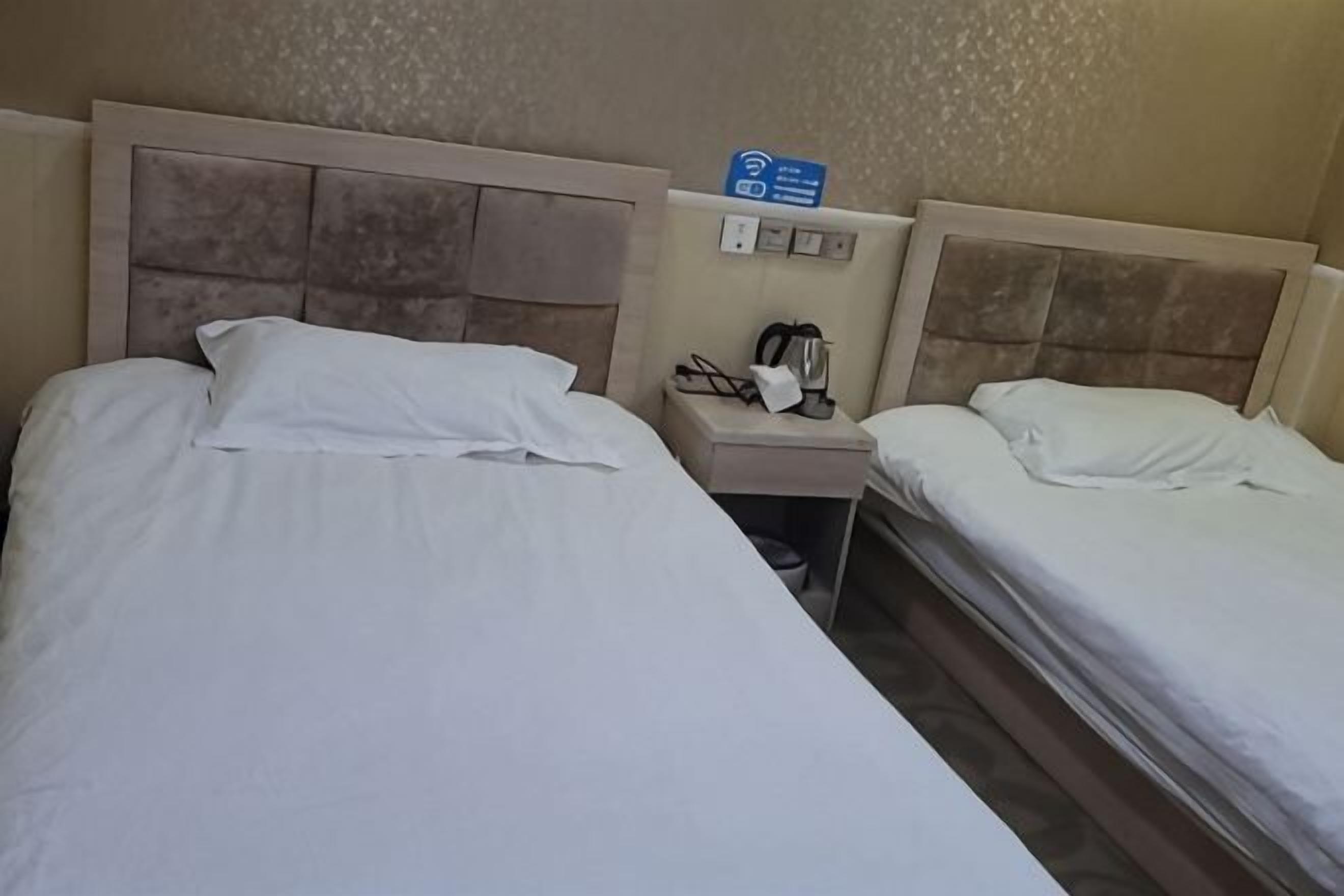 A hotel room with two beds, a nightstand with a phone and a coffee maker, and a sign indicating Wi-Fi availability.