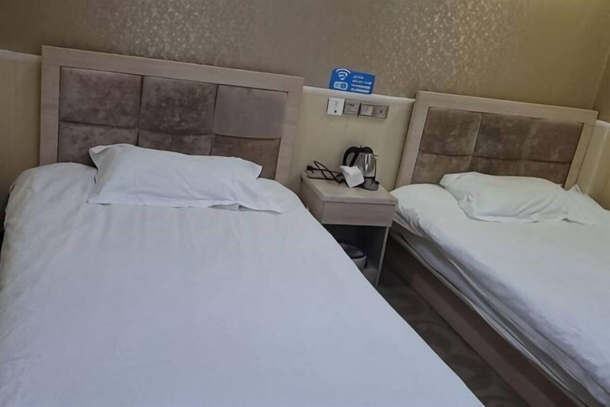 A hotel room with two beds, a nightstand with a phone and a coffee maker, and a sign indicating Wi-Fi availability.