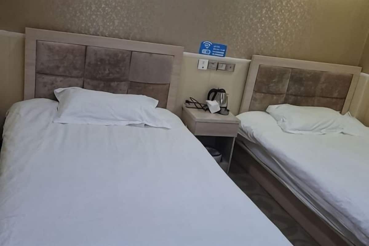A hotel room with two beds, a nightstand with a phone and a coffee maker, and a sign indicating Wi-Fi availability.