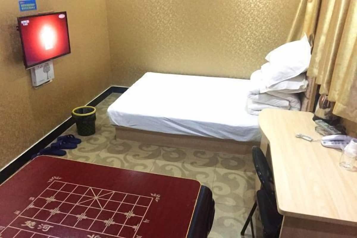 A hotel room with a bed, a desk, a television, and a small trash bin.