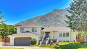 A two-story house with a garage, a front porch, and a mountain backdrop. - Sandy East Bench • Pool • Mountain Views • Hot Tub (Sandy)