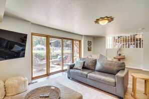 A living room with a grey sofa, a television mounted on the wall, and a large sliding glass door leading to an outdoor area. - Sandy East Bench • Pool • Mountain Views • Hot Tub (Sandy)