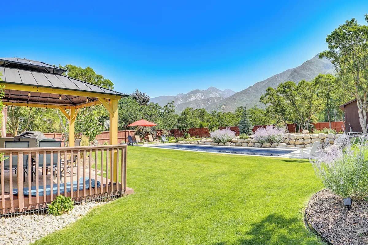 A backyard with a wooden deck, a barbecue area, a swimming pool, and a mountain view.