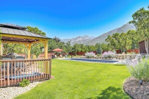 A backyard with a wooden deck, a barbecue area, a swimming pool, and a mountain view.