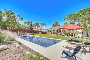 A backyard with a swimming pool, lounge chairs, and a red umbrella. - Sandy East Bench • Pool • Mountain Views • Hot Tub (Sandy)