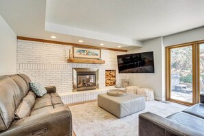 Ein Wohnzimmer mit Kamin, einer Couch, Poufs und einem an der Wand befestigten Fernseher.