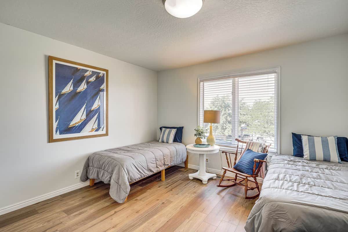 Un dormitorio con dos camas, una mesita, un sillón mecedor y una ventana con persianas.
