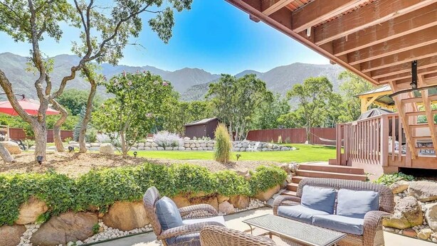 An outdoor patio with wicker furniture, a stone wall, and a view of mountains. - Sandy East Bench • Pool • Mountain Views • Hot Tub (Sandy)