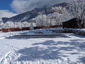 A snow-covered outdoor area with a stone wall, a wooden fence, and a building in the background. - Sandy East Bench • Pool • Mountain Views • Hot Tub (Sandy)