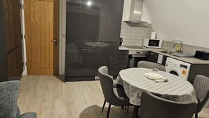 A compact kitchen with a microwave, oven, and a small dining area with a table and chairs. - Affordable 2 bedroom flat in Bedford (Bedford)