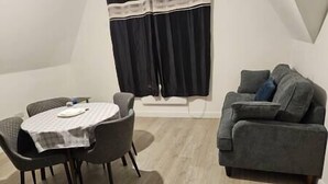 Una habitación con una mesa de comedor, sillas, un sofá gris y una ventana con cortinas negras.