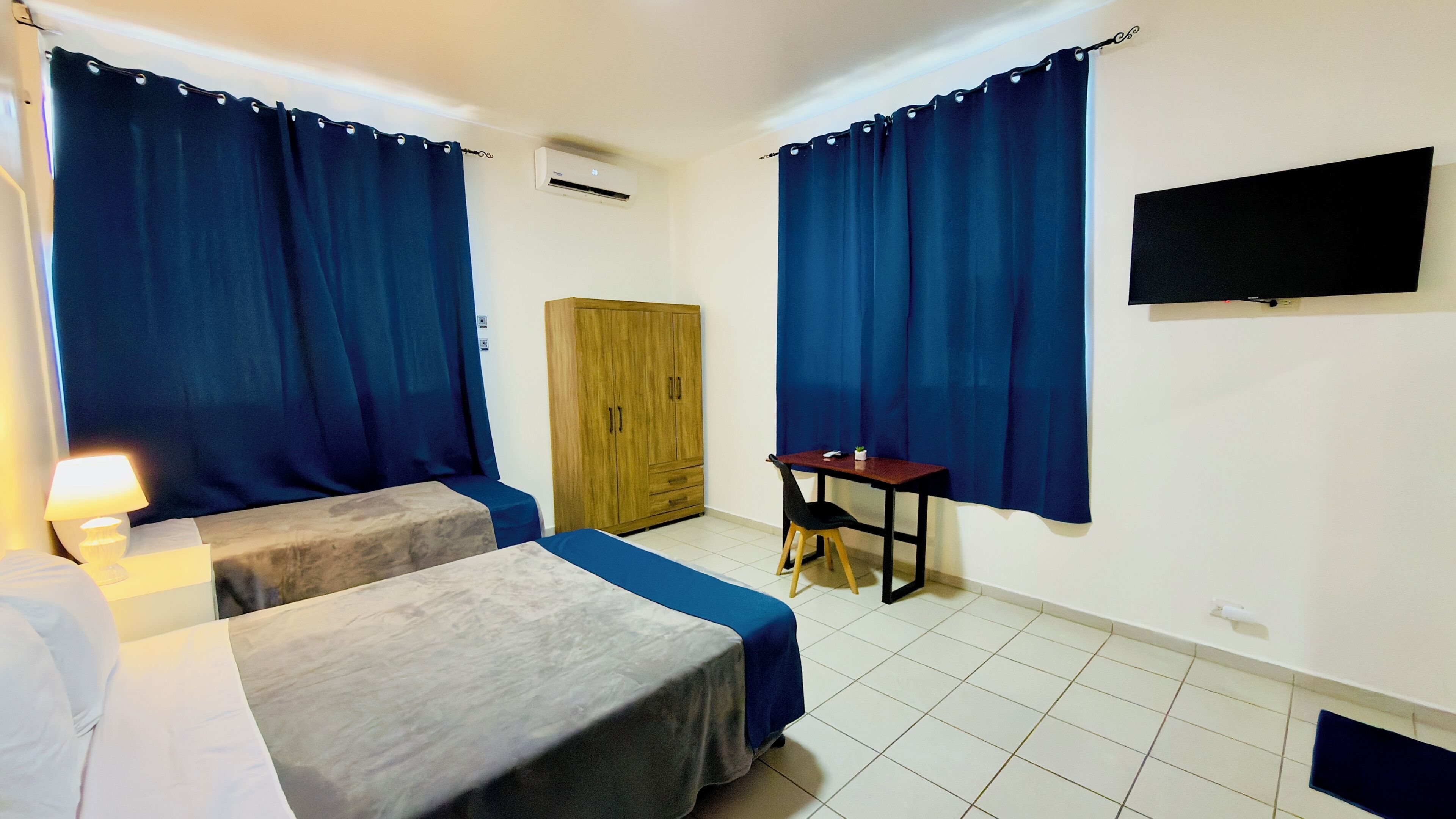 A room with two beds, a wooden wardrobe, a desk, and a TV mounted on the wall.