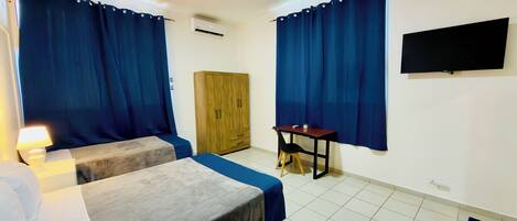 A room with two beds, a wooden wardrobe, a desk, and a TV mounted on the wall.