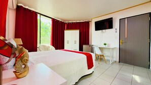 Habitación de hotel con cama, escritorio, televisor, armario y ventana con cortinas.