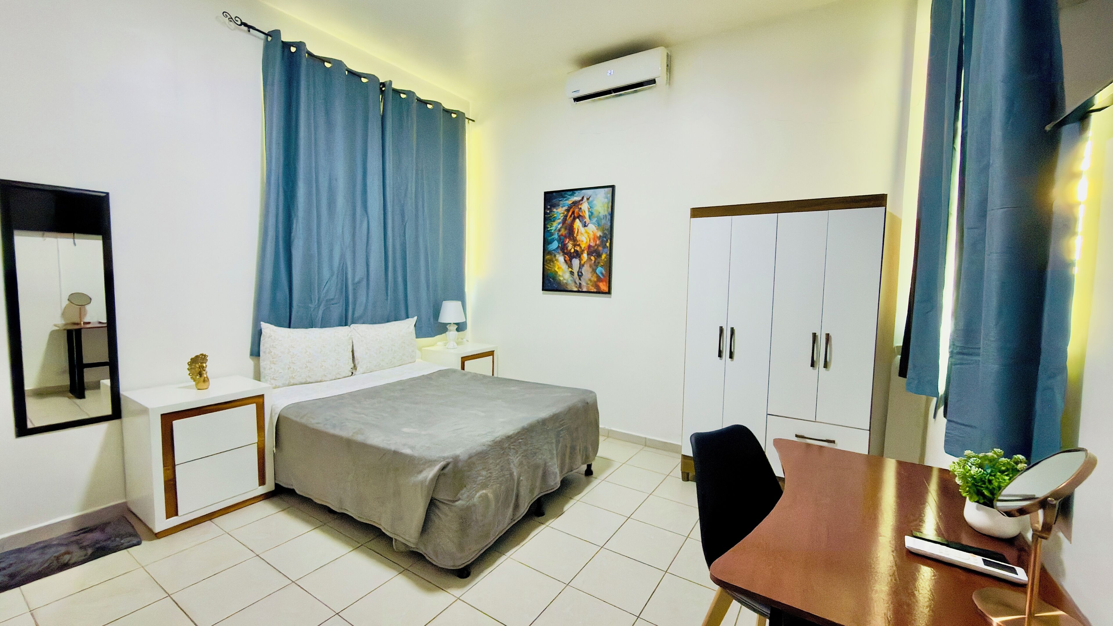Habitación de hotel con cama, mesitas de noche, escritorio, silla, espejo, armario y equipo de aire acondicionado.