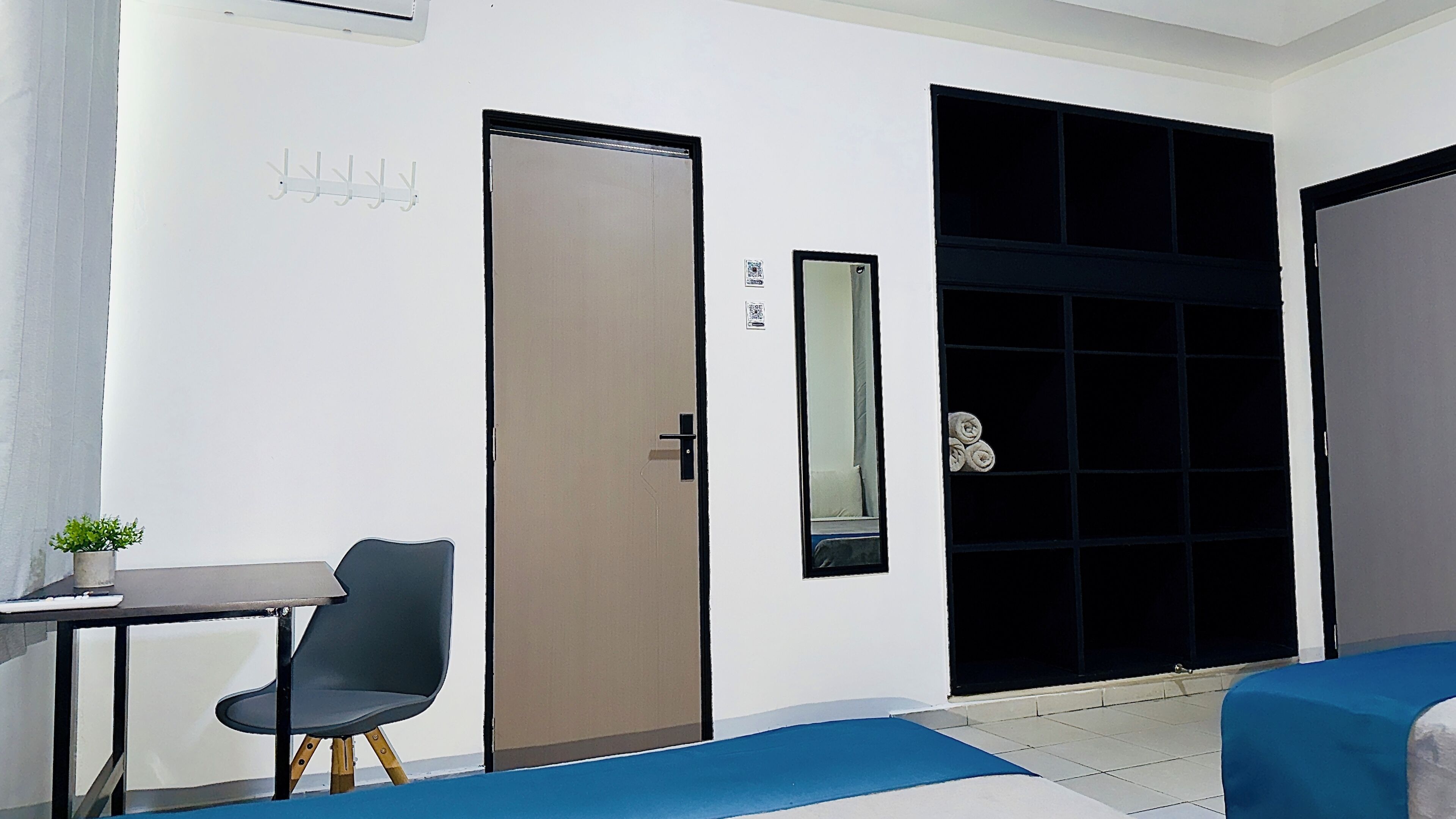 Una habitación con escritorio, silla, dos camas, una puerta y una planta pequeña.