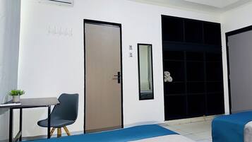 Una habitación con escritorio, silla, dos camas, una puerta y una planta pequeña.