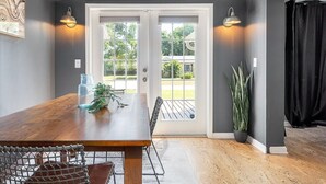 Un coin repas avec une table et des chaises en bois, un vase en verre contenant une plante, et une vue sur l’extérieur à travers des portes vitrées.