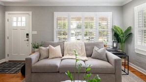 Un salon avec un canapé beige, une porte blanche et une fenêtre avec des stores.