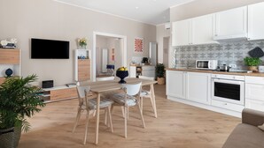 A modern kitchen with white cabinets, a microwave, and a stove. There is a dining area with a wooden table and chairs. - Maison MimìMarì - Sorrento City Center (Sorrento)